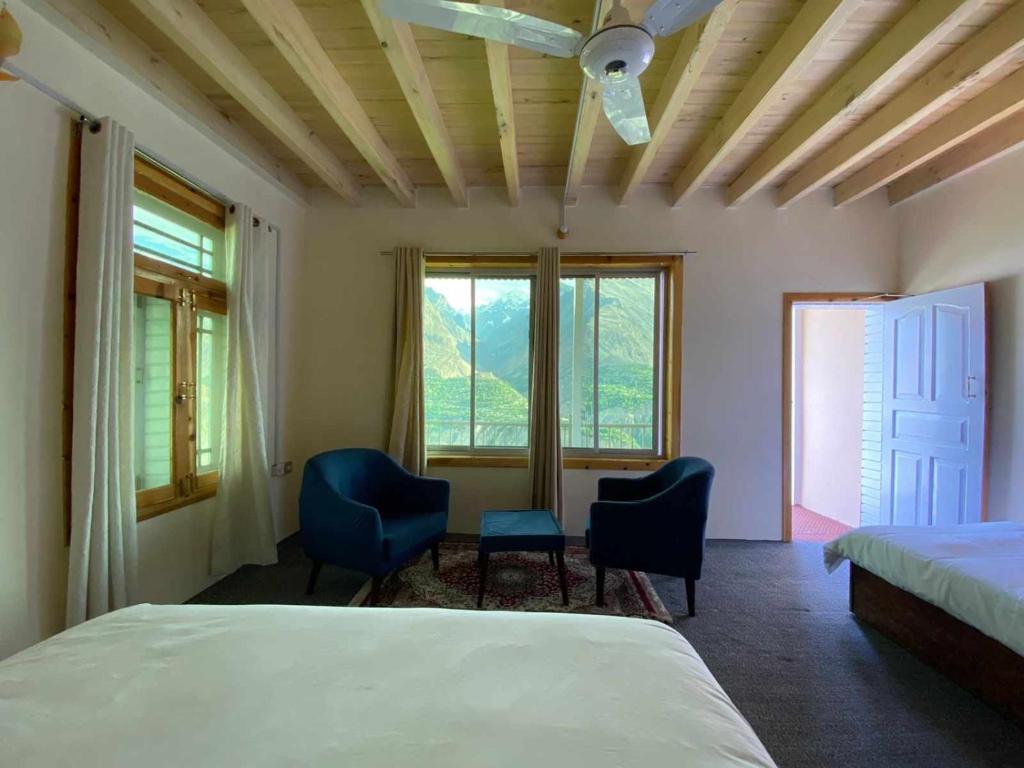 Schlafzimmer mit 2 Stühlen, einem Bett und Fenstern in der Unterkunft Hunza Lounge in Hunza
