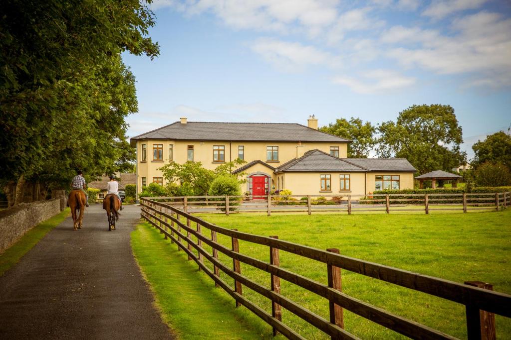 una persona montando un caballo por un camino delante de una casa en Cahergal Farmhouse B&B en Newmarket on Fergus