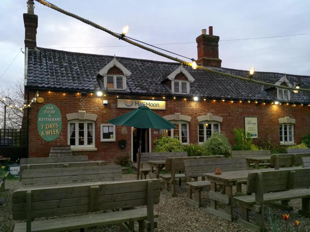 a restaurant with wooden benches in front of a brick building at The Half Moon Inn Rushall IP21 4QD in Pulham Saint Mary the Virgin