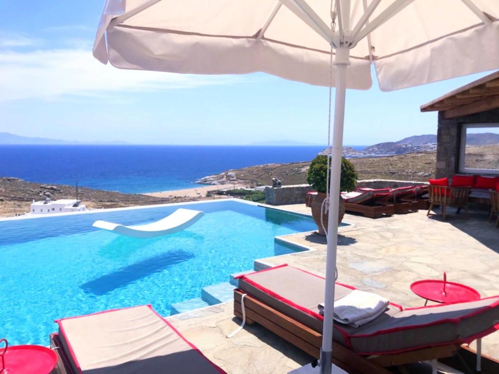 uma piscina com cadeiras e um guarda-sol e o oceano em VILLA NAUTILIA - Luxury Suites and Cottages em Kalafatis