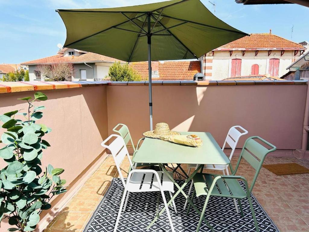 ein grüner Tisch und Stühle mit einem Sonnenschirm auf einer Terrasse in der Unterkunft La casa magique, bulle enchantée, 100m de la plage in Andernos-les-Bains
