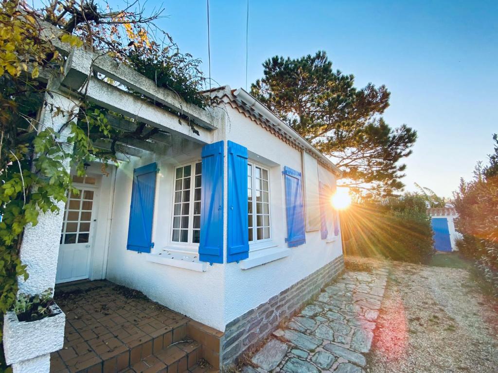 une maison blanche avec des fenêtres bleues et le soleil brillant dans l'établissement Le brisou 400 m de la plage quartier Boisvinet, à Saint-Gilles-Croix-de-Vie