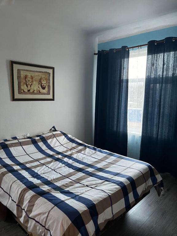 1 dormitorio con 1 cama con cortinas azules y ventana en Dzērves apartamenti, en Nastrova