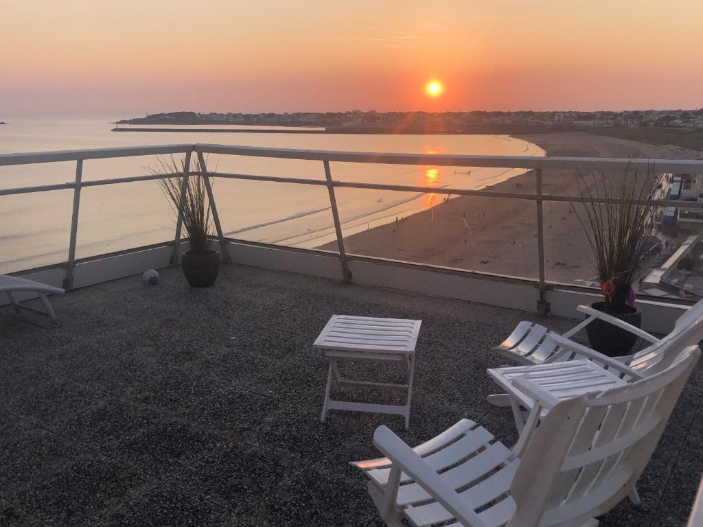 2 chaises et une table sur un balcon avec un coucher de soleil dans l'établissement Le Rêve bleu, à Saint-Gilles-Croix-de-Vie