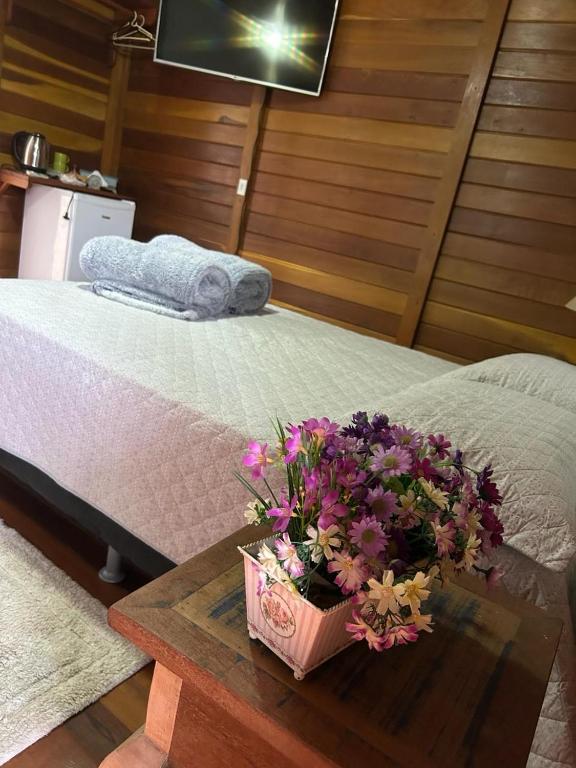 a bedroom with a bed with a table with flowers on it at Chalé Ipê Branco in Pedra Azul