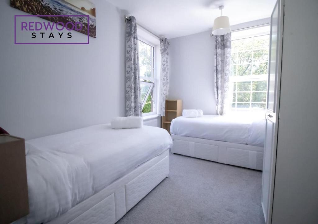 a white bedroom with two beds and a window at Spacious Serviced Apartment for Contractors and Families, FREE WiFi & Netflix by REDWOOD STAYS in Farnborough