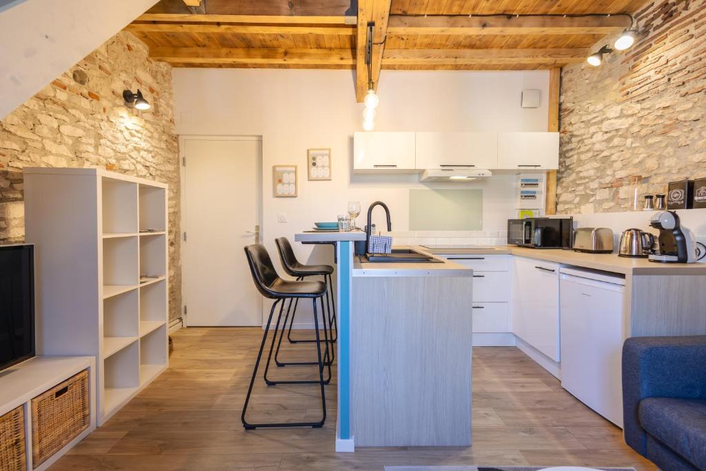 een keuken met witte kasten en een bar met krukken bij L'alouette - Duplex Climatisé & Authentique in Castres