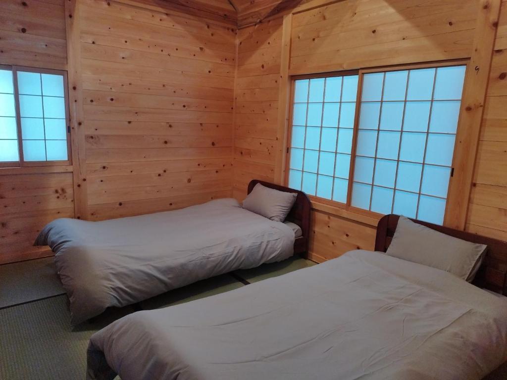 two beds in a room with wooden walls and windows at Country Resort Sugou - Vacation STAY 41071v in Hida