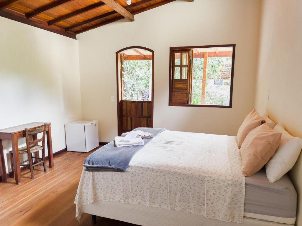 a bedroom with a bed and a table and two windows at Pousada da Fonte in Lençóis