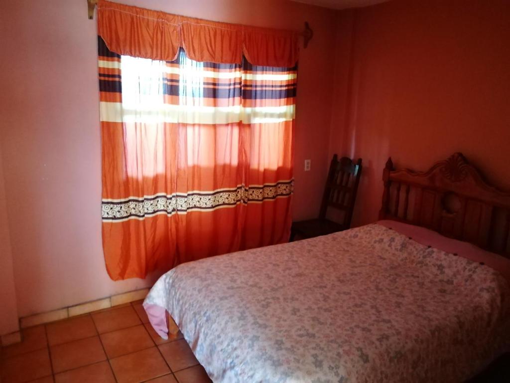 a bedroom with a bed and a window with an orange curtain at El Mesón de Don Quijote in Mazamitla
