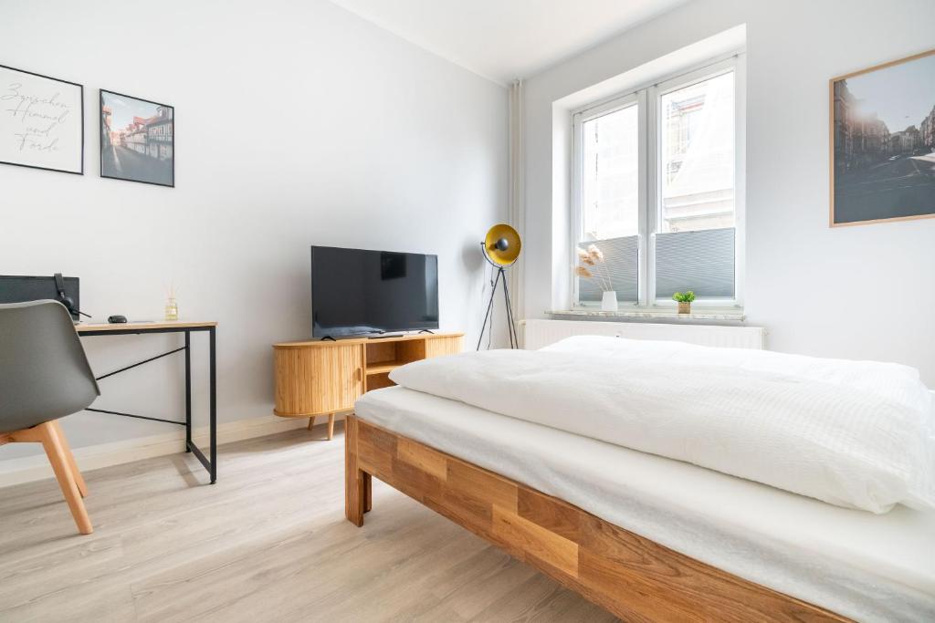 a white bedroom with a bed and a desk and a tv at Zentrales Apartment am Nordertor in Flensburg