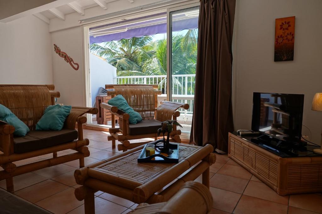 a living room with chairs and a television and a balcony at LE CALYPSO BORD DE MER in Les Trois-Îlets