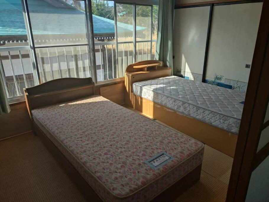 a room with two beds and a balcony with windows at 名高儀の宿 in Iwaki