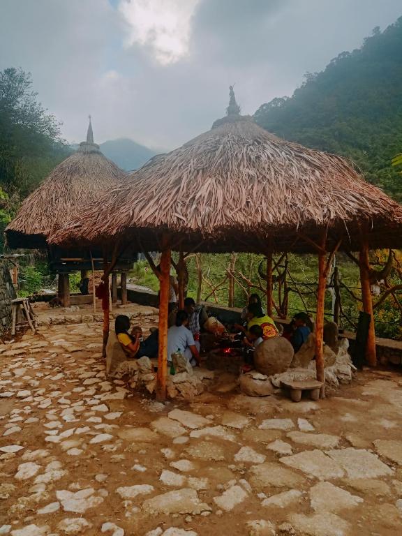 um grupo de pessoas sentadas debaixo de uma cabana de palha em Agamang Traditional House Inn em Banaue