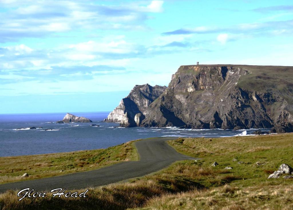 uma estrada de terra junto ao oceano com uma montanha em John Eoinìn's Bar and accommodation em Glencolumbkille