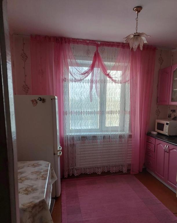 Habitación con una ventana con cortinas rosas y microondas. en Квартира, en Pavlodar