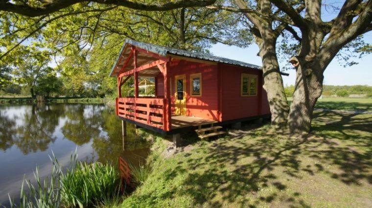 una casa roja sentada a un lado de un lago en Vakantiepark Vlinderloo en Enschede