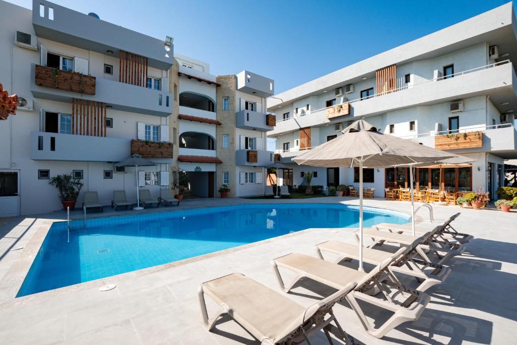 una piscina con sillas y una sombrilla junto a un edificio en Dimitra Hotel & Apartments by Omilos Hotels, en Kokkíni Khánion