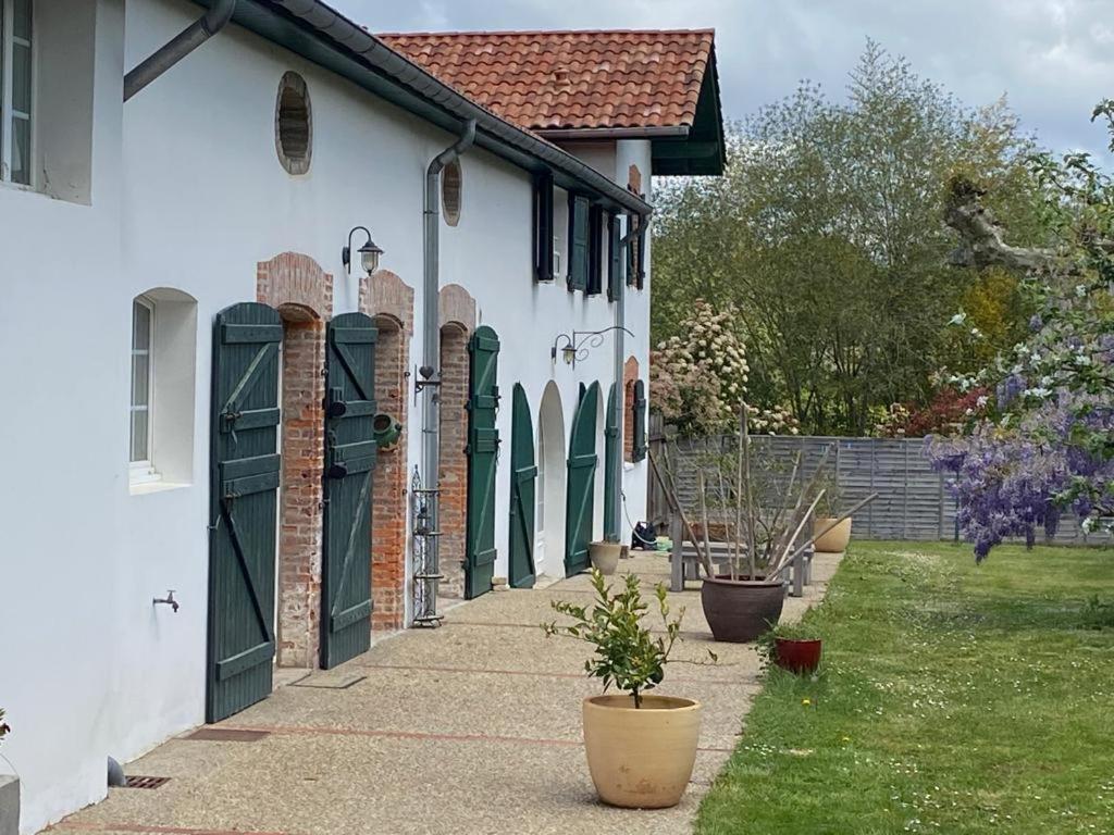 una casa bianca con porte verdi e un cortile di Chambres d'hôtes Maison Narbay aux portes du pays Basque a Saint-André-de-Seignanx