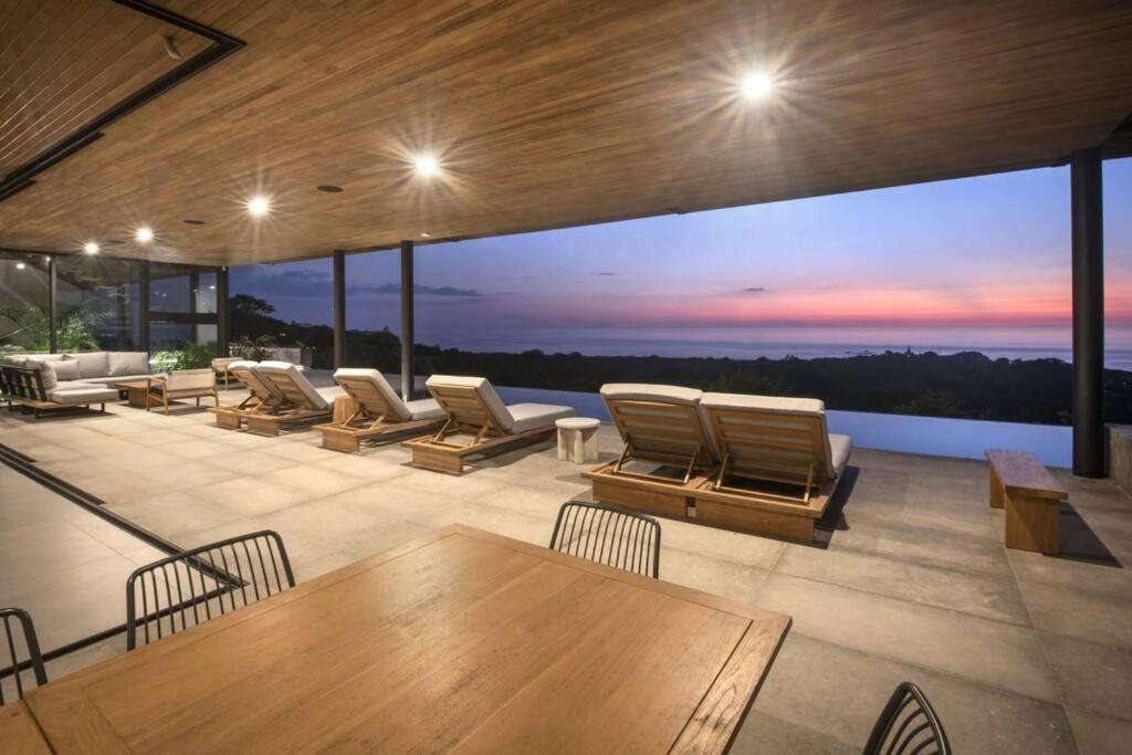 eine Terrasse mit Liegestühlen, Tischen und Sonnenuntergang in der Unterkunft Casa Con Vista – Nosara, Guanacaste, Costa Rica. S in Nosara