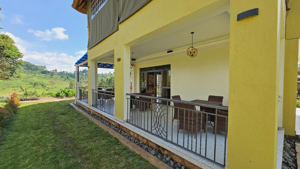 a yellow house with a balcony with a table and chairs at Kaije Country Cottages in Fort Portal