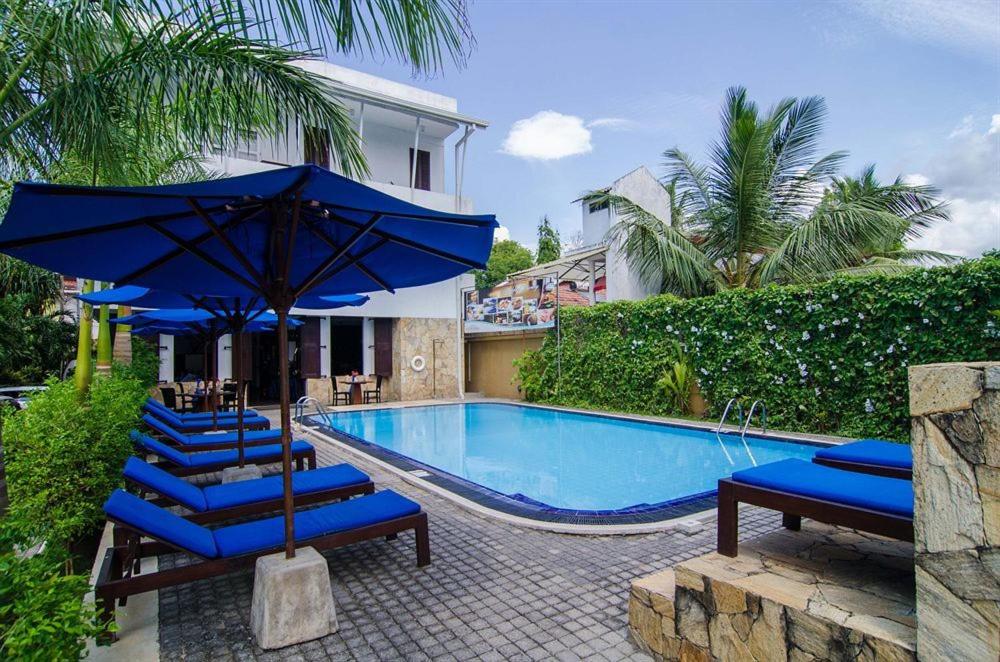 a swimming pool with blue lounge chairs and an umbrella at St.Lachlan Hotel & Suites in Negombo