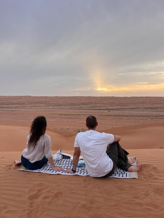 a man and woman sitting on a blanket in the desert at Marbella bungalows desert in Bidiyah