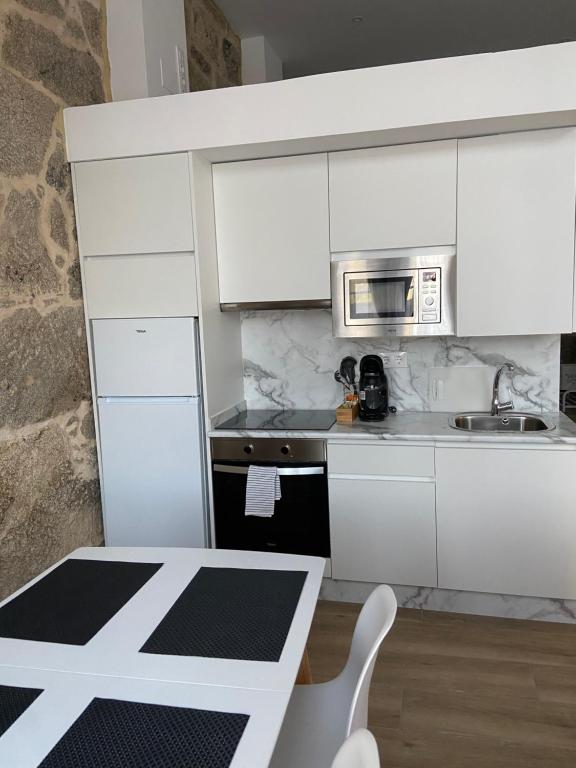 cocina con armarios blancos, mesa y microondas en Reginita Apartamentos, en Arbo