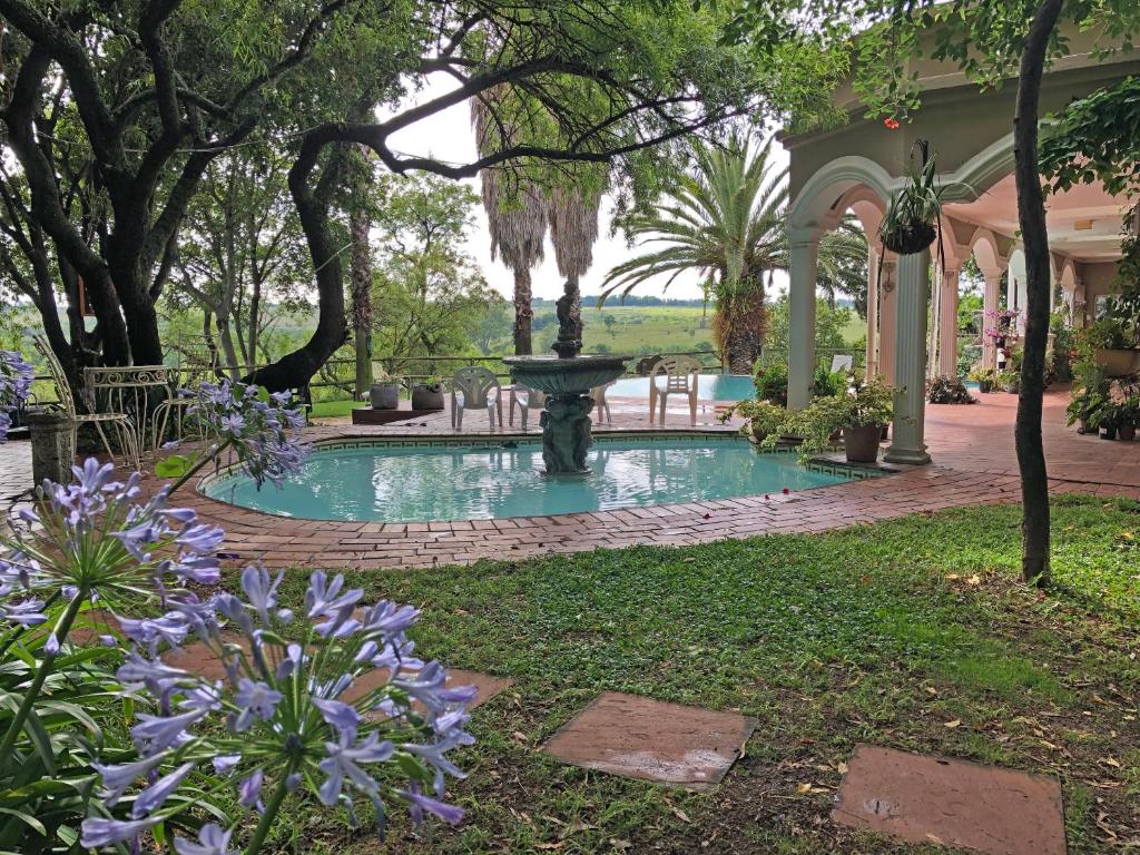 a fountain in a garden with trees and purple flowers at Hills and Dales Accommodation in Lanseria