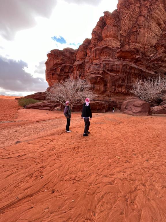 duas pessoas caminhando no deserto perto de uma formação rochosa em Mars moon camp em Wadi Rum