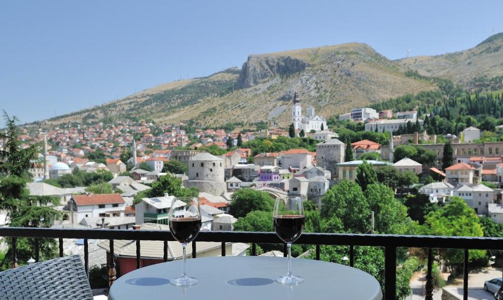 two glasses of wine sitting on a balcony with a city at Captain's Luxury Apartments in Mostar