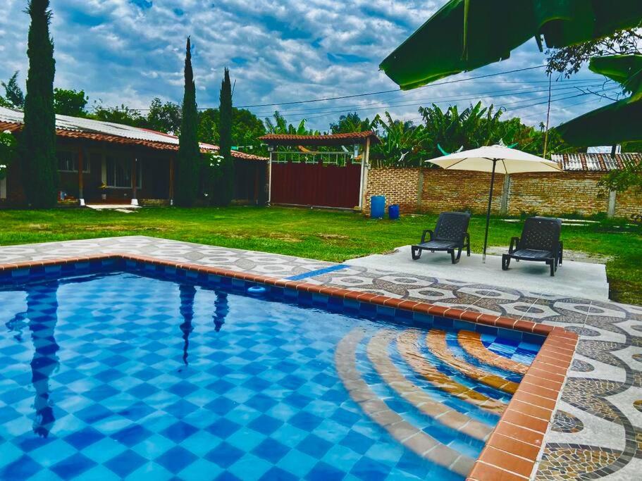 a swimming pool in a yard with two chairs and an umbrella at Finca Rozo in Palmira