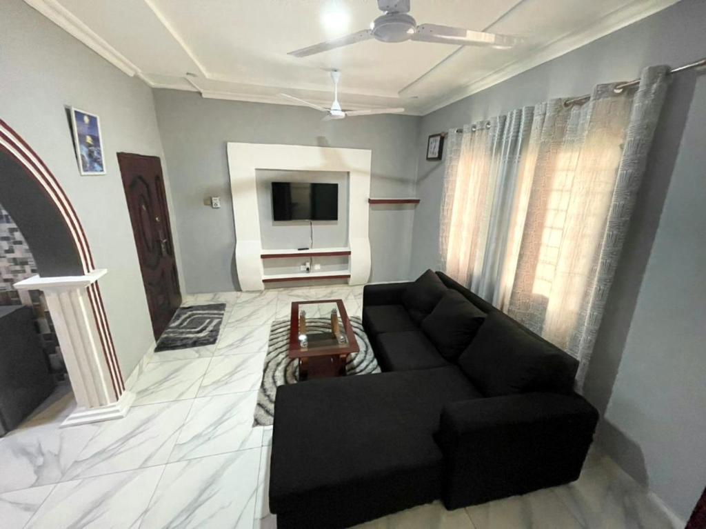 ein Wohnzimmer mit einem schwarzen Sofa und einem TV in der Unterkunft Accra City Apartments in Accra