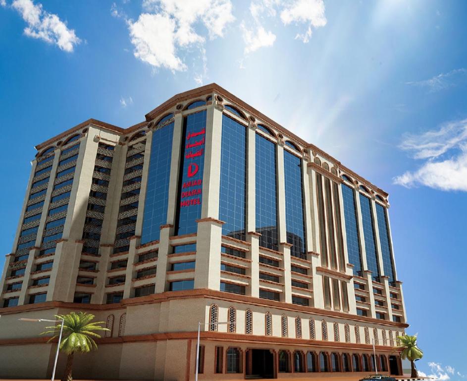 a large building with blue windows and a palm tree at Amjad Al Deafah Hotel in Makkah