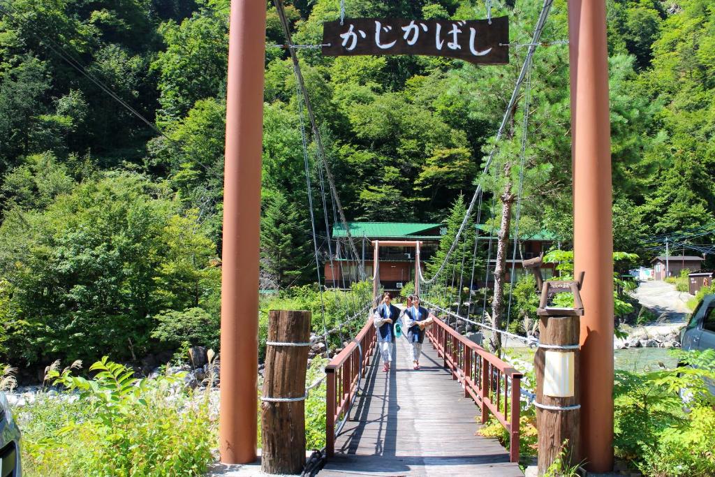 a suspension bridge over a river with people walking on it at Shinzanso in Takayama