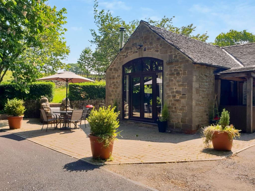 a building with a patio with a table and an umbrella at Waterfall Cottage in Tansley