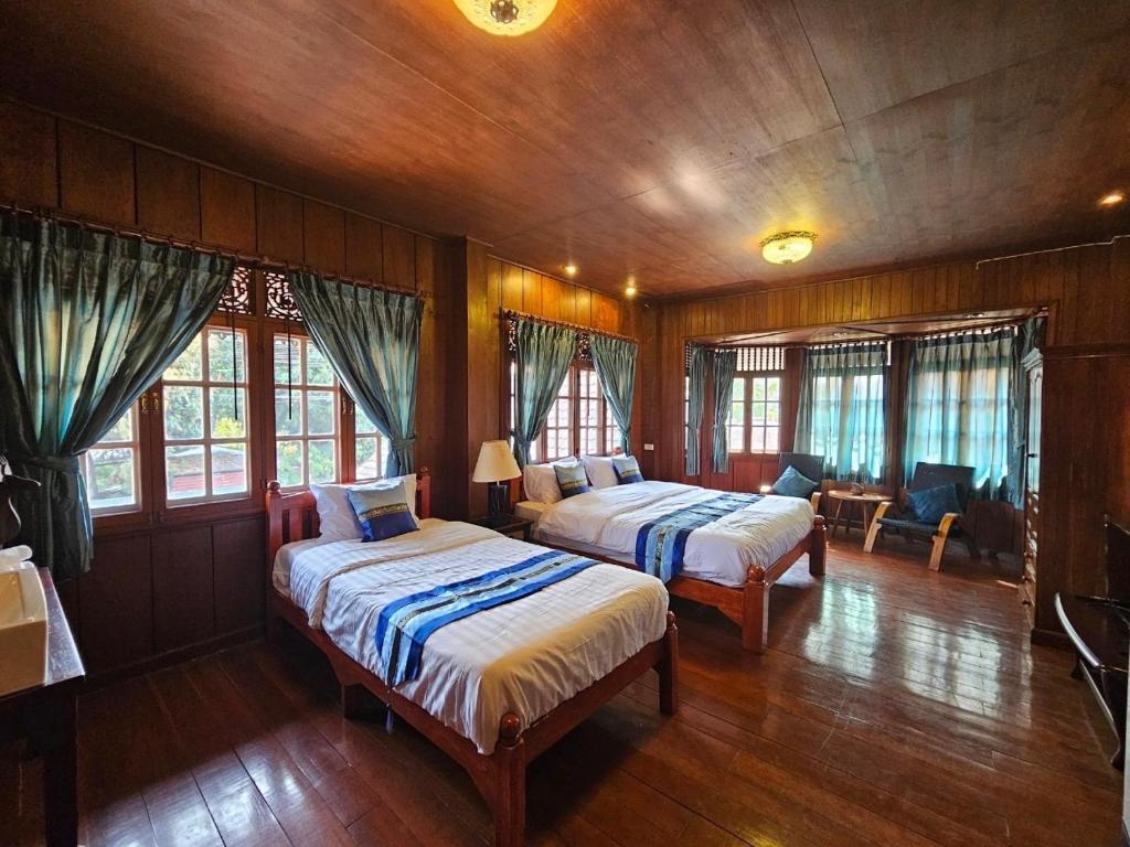 two beds in a room with wooden walls and windows at Malulee Homestay/Cafe/Massage in Lampang