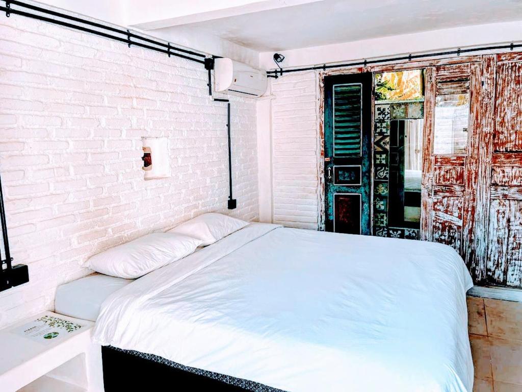 ein weißes Bett in einem Zimmer mit Ziegelwand in der Unterkunft Bingin Bienvenue Guest House in Uluwatu