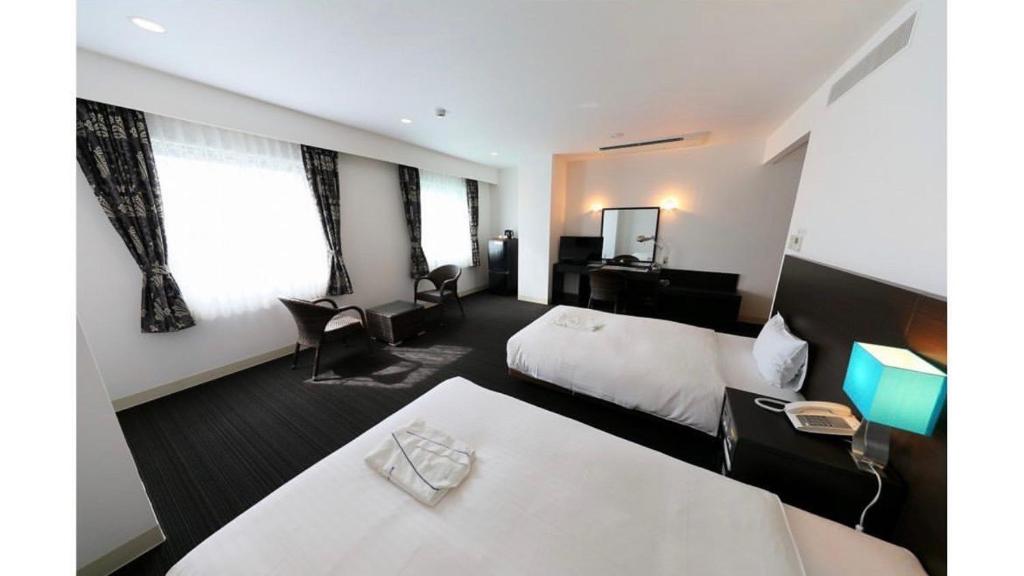 Habitación de hotel con 2 camas y escritorio en Libest Inn Amami, en Setouchi