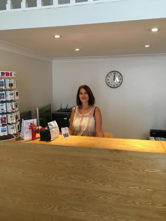 une femme debout derrière un comptoir avec une horloge dans l'établissement Melbourne House Hotel, à Londres