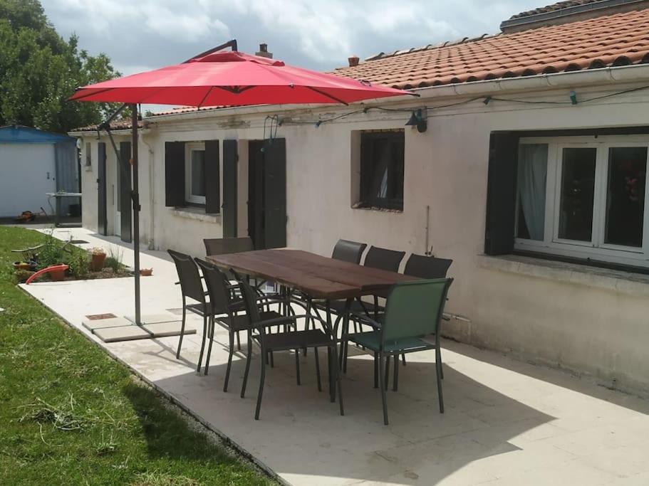 une table et des chaises en bois avec un parapluie rouge dans l'établissement Longère charentaise familiale., à La Tremblade