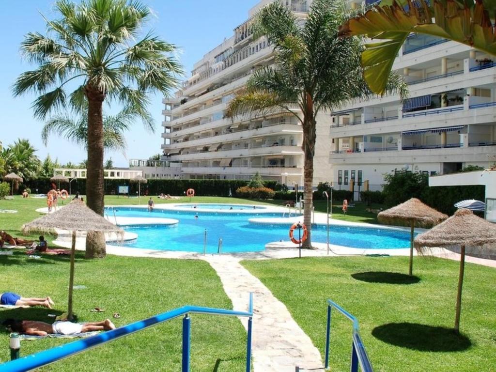 a swimming pool with palm trees and a large building at Apartamento Las Terrazas ll in Marbella