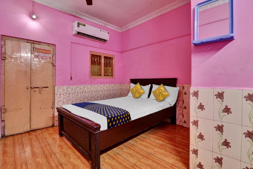 a bedroom with pink walls and a bed with yellow pillows at SPOT ON Sri Maheswari Lodge in Vijayawāda