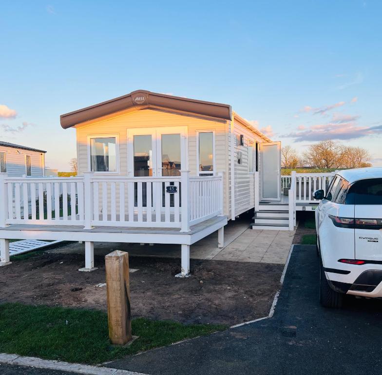 a white tiny house with a car parked in front at The Pastures Holiday Lodge in Tattershall