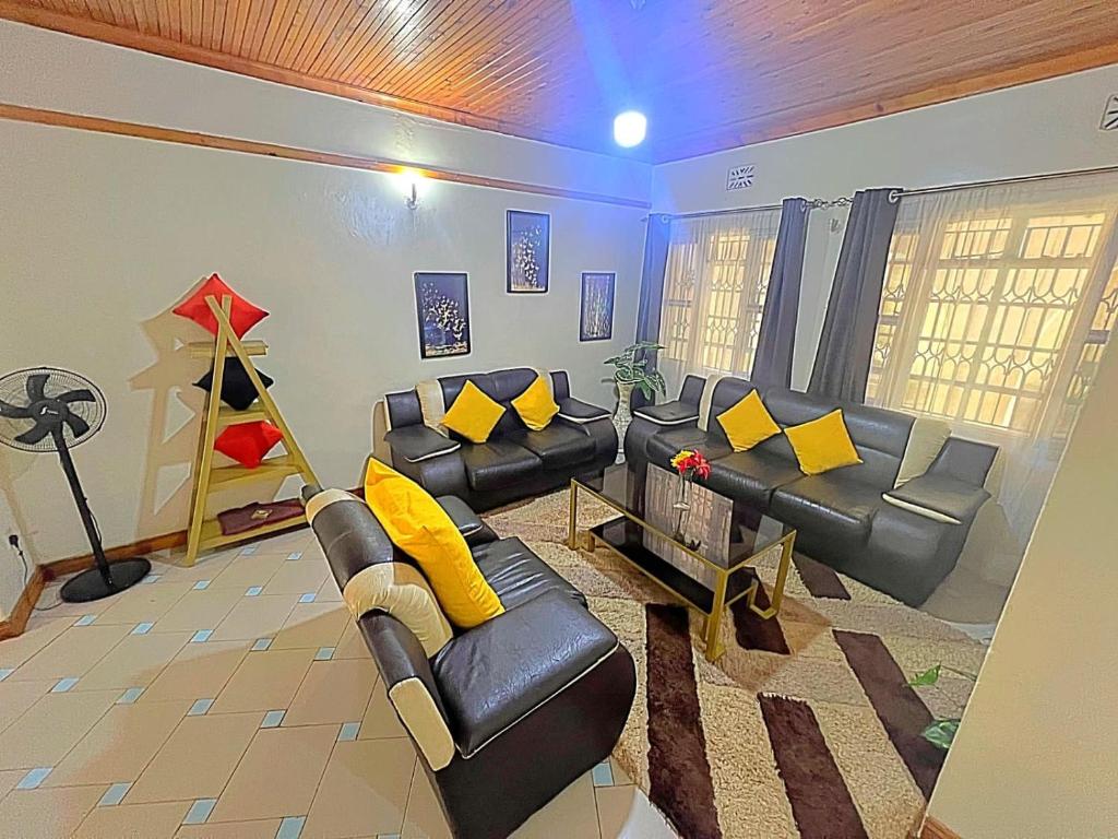 uma sala de estar com mobiliário de couro preto e almofadas amarelas em Homely apartments 4 em Kisumu