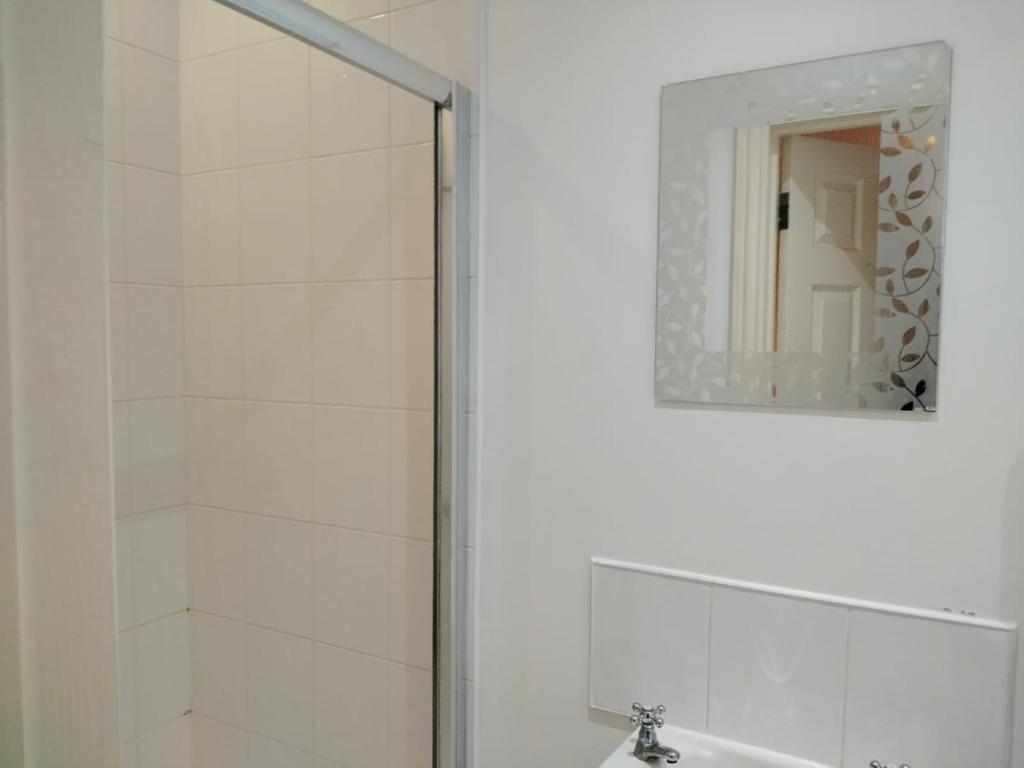 a white bathroom with a shower and a mirror at Thales Home GFDBL1 in Barking