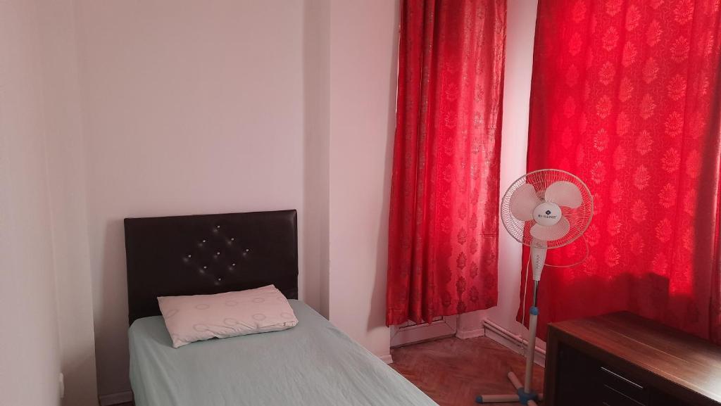 um quarto com uma cama com cortinas vermelhas e uma ventoinha em Şirinevler Guest house em Istambul