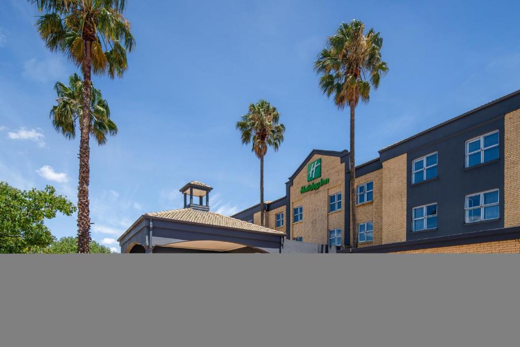 肯普顿帕克Holiday Inn Johannesburg OR Tambo Airport Hotel by IHG的建筑物前的一排棕榈树