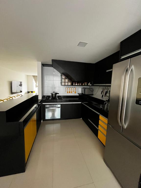 a kitchen with black and yellow cabinets and a stainless steel refrigerator at Village 3/4 a 140m da praia in Ilhéus