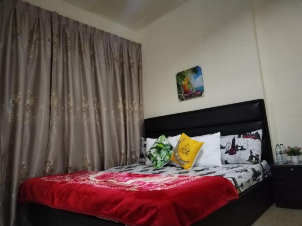1 dormitorio con 1 cama con sábanas rojas y almohadas amarillas en My Home Stay Apartment, en Abu Dabi